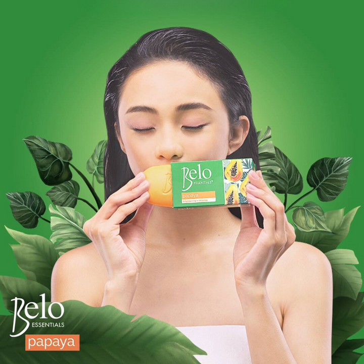 Woman holding a Belo Papaya soap bar against a green background with leaves.