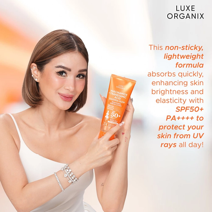 Woman holding a Luxe Organix sunscreen bottle with product details on a light background