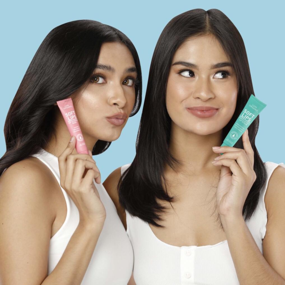 Two women holding skincare products against a blue background