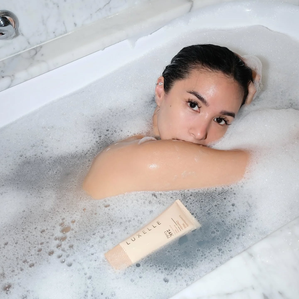 Woman in a bathtub with bubbles and a tube of Luxelle product.