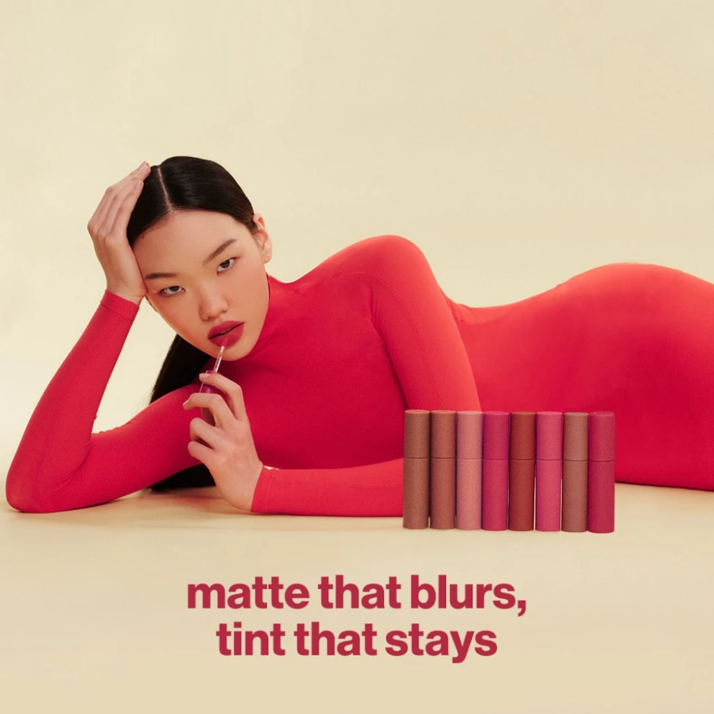 Woman in red outfit with makeup products on a beige background Sunnies Face Lip Dip - Aura