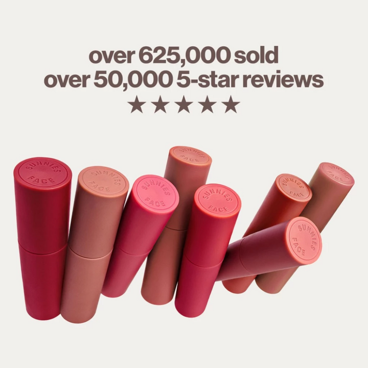 Collection of red and pink lipsticks with brand name on a white background, featuring text about sales and reviews. Sunnies Face Lip Dip - Aura