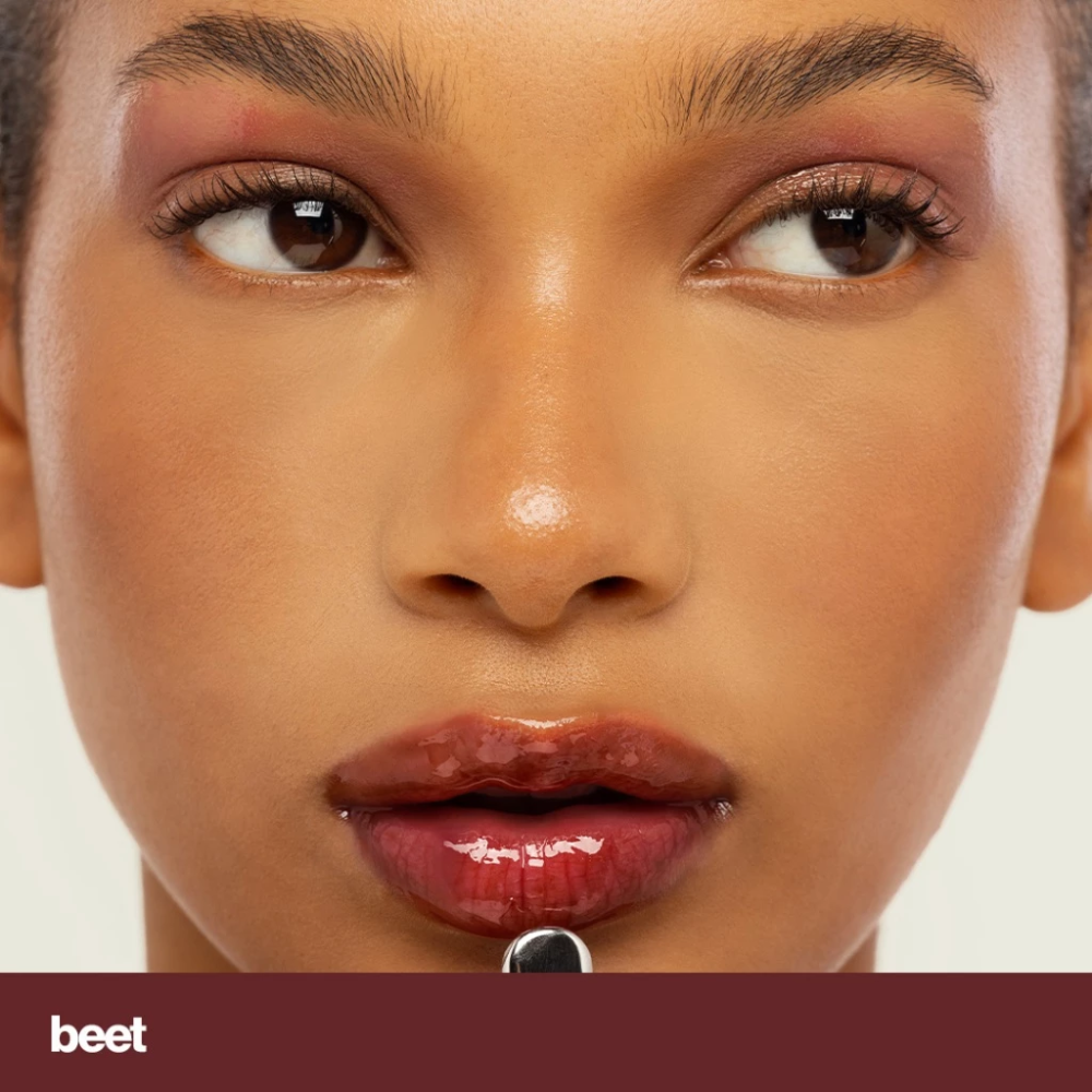 Close-up of a woman's face with a neutral background, featuring the shade 'beet'. Sunnies Face Lip Glaze - a peptide lip treatment