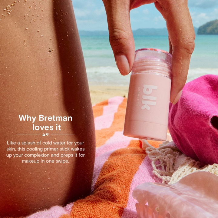Person holding a pink skincare stick with a beach background Blk Cosmetics Cooling Primer Stick