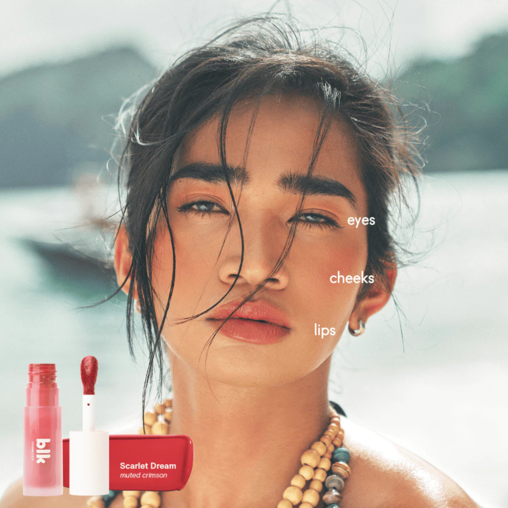 Woman with makeup products labeled 'eyes', 'cheeks', and 'lips' on a blurred natural background Blk Cosmetics Creamy All-Over Paint - Pink Cloud