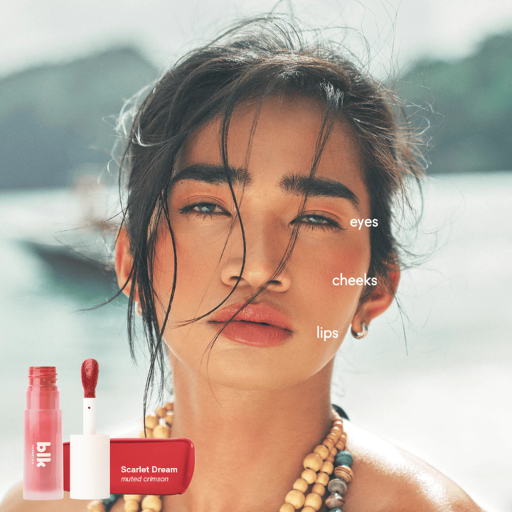 Woman with makeup products labeled 'eyes', 'cheeks', and 'lips' on a blurred natural background Blk Cosmetics Creamy All-Over Paint - Pink Cloud